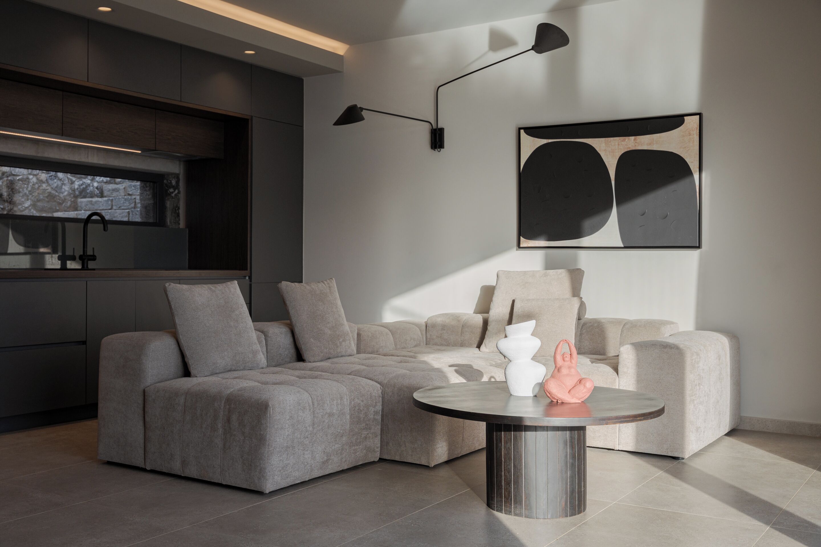 A modern living room with a sectional sofa, a round coffee table, and a minimalist art piece on the wall.