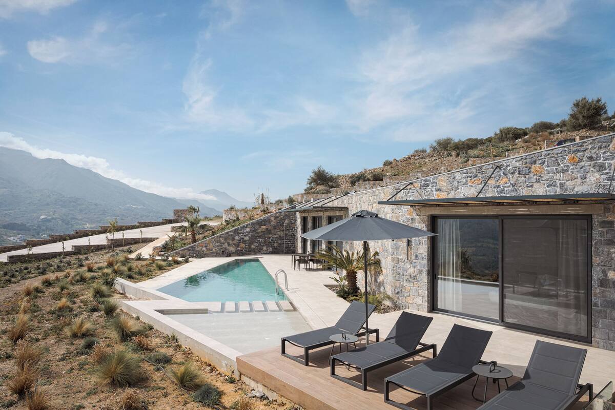 A modern outdoor pool area with lounge chairs and a stone building with large windows.