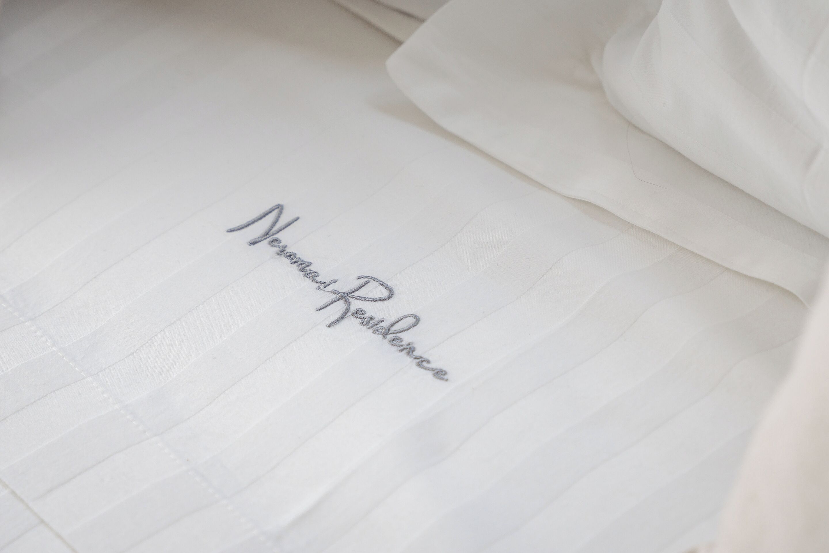 A neatly made bed with a pillow and a piece of paper with the words "Nomadic Residence" written on it.