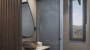 A modern bathroom with a wooden vanity, a large mirror, a glass shower enclosure, and a view of the outdoors through a window.