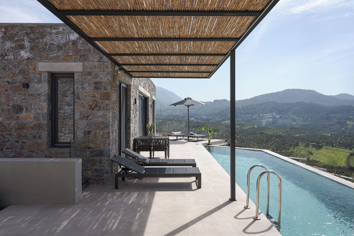 A modern outdoor pool area with stone walls, lounge chairs, and a view of the mountains.
