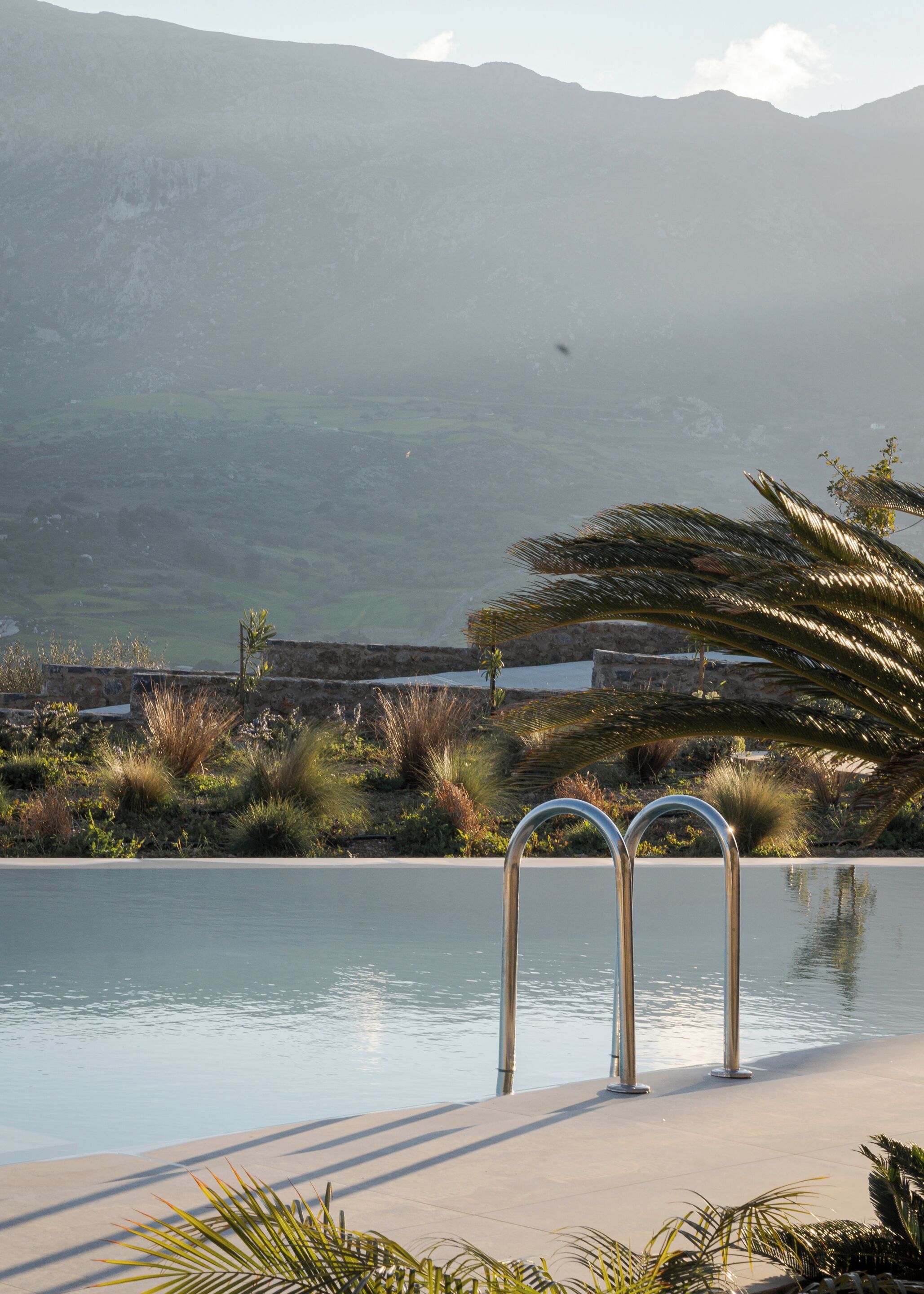 Une piscine entourée de plantes tropicales et bordée de rampes métalliques, avec une chaîne de montagnes en toile de fond.