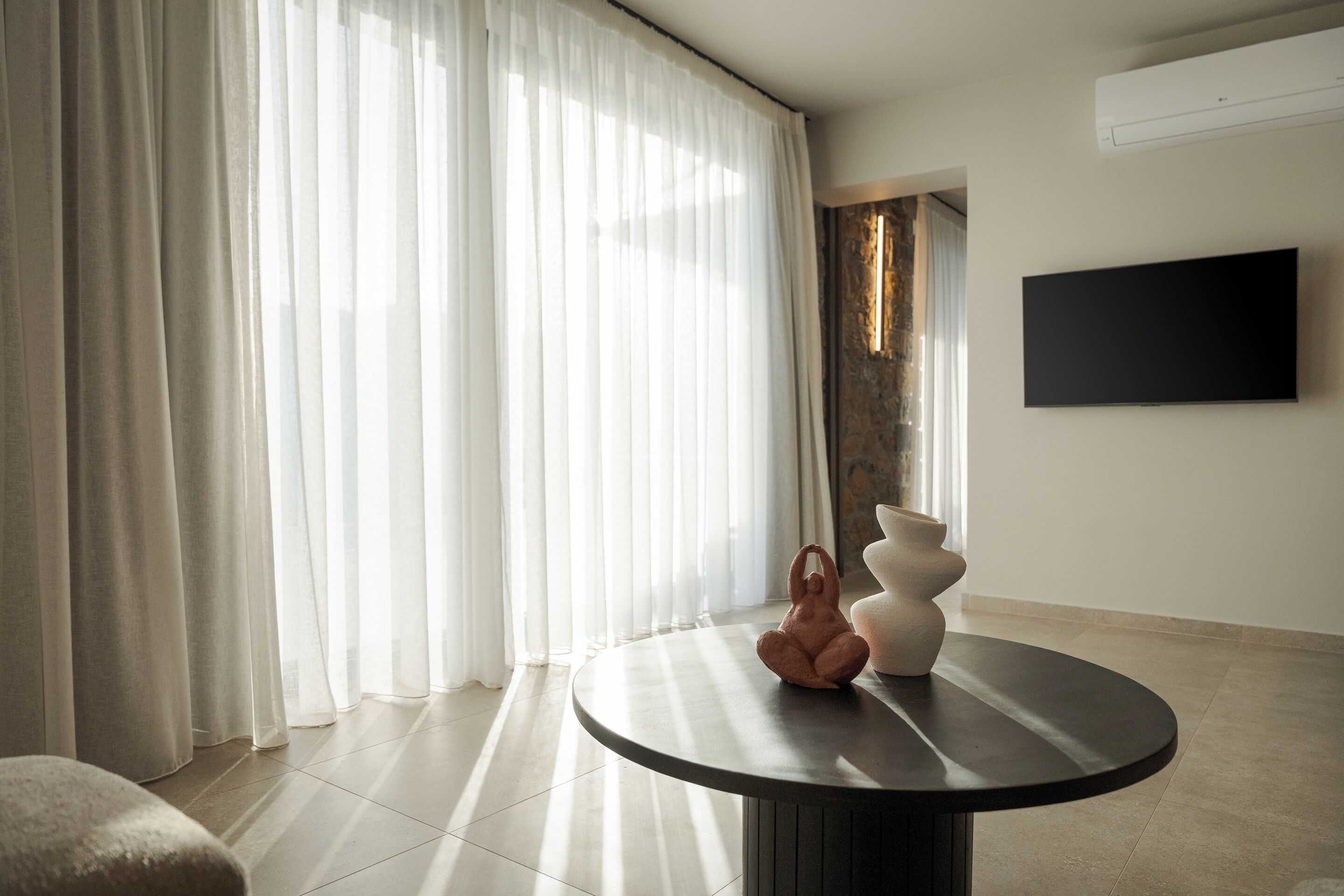 Een moderne woonkamer met een ronde tafel, een decoratief beeldhouwwerk en een flatscreen televisie aan de muur.
