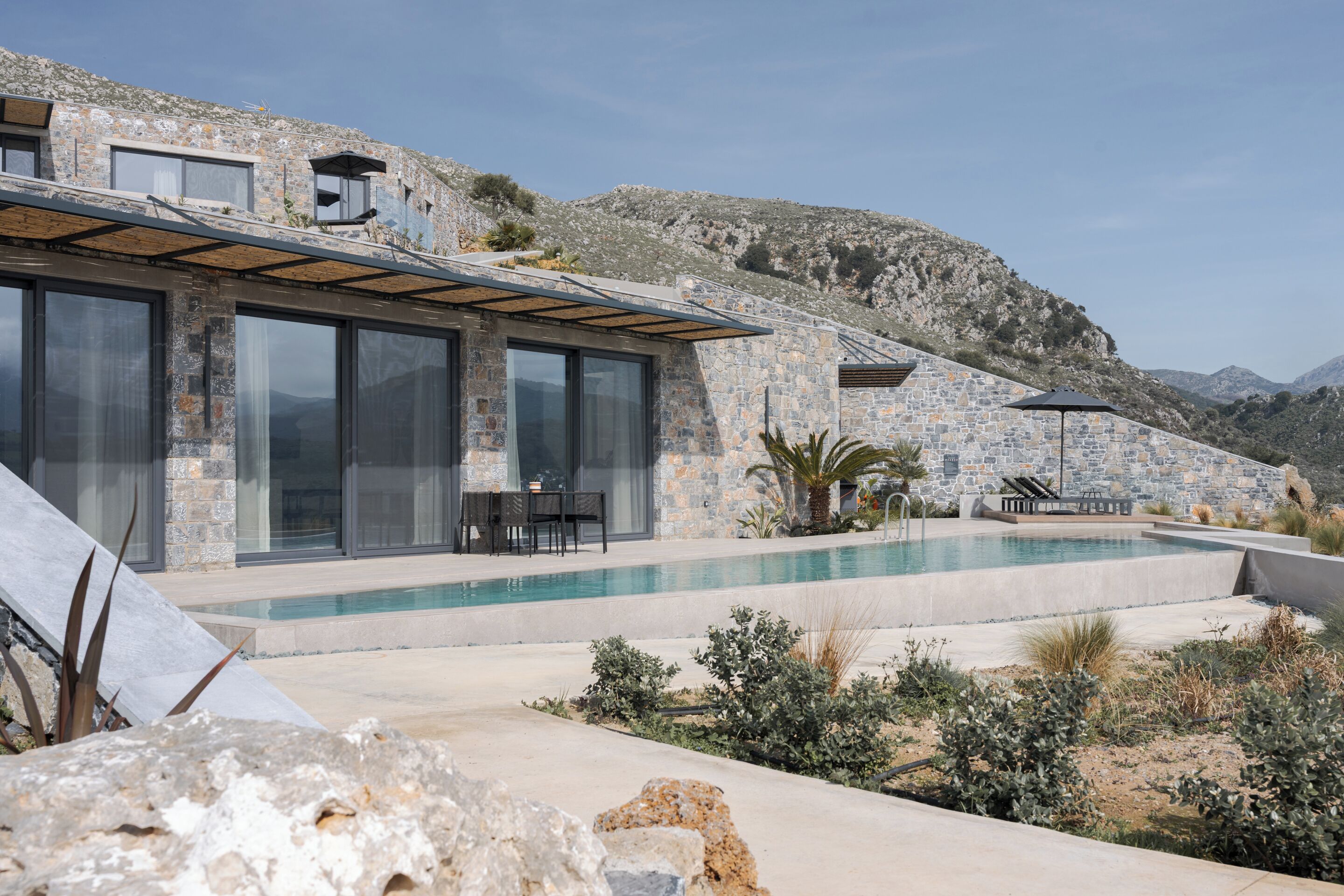 A modern house with a stone exterior, a swimming pool, and a patio area with outdoor furniture.