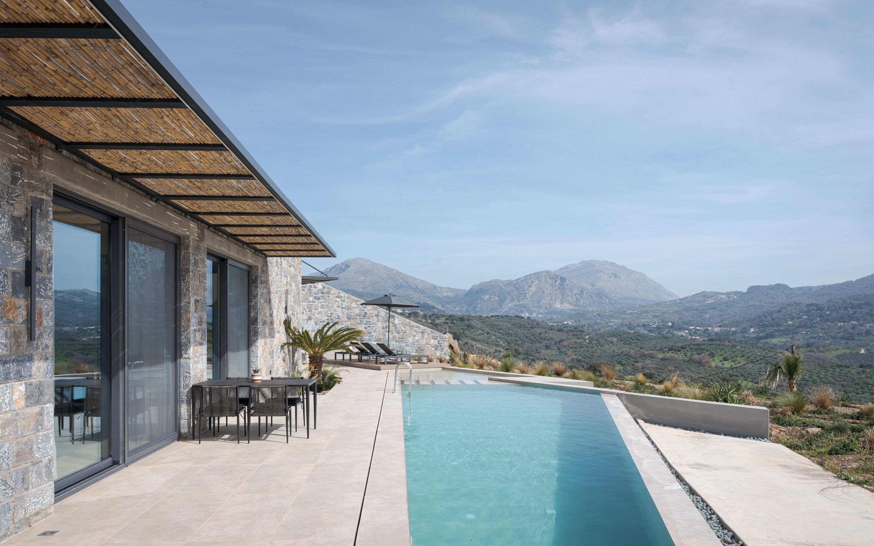 Un bâtiment moderne avec une façade en pierre, une piscine, un espace extérieur aménagé et une vue sur les montagnes.