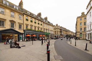 A street with buildings, a sidewalk, and a few people.