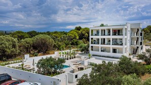 Un immeuble moderne à plusieurs étages, doté de balcons, d’une piscine et entouré de verdure.