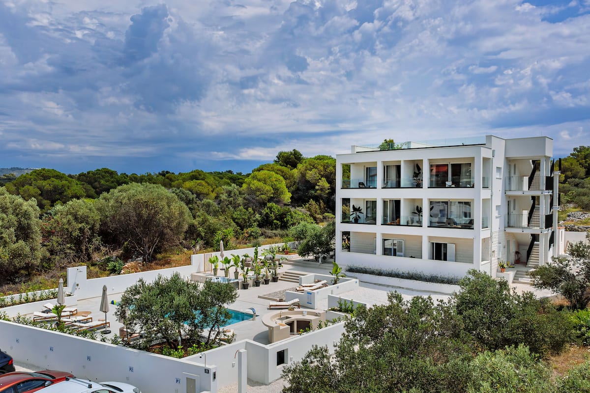 A modern multi-story building with balconies, a swimming pool, and surrounding greenery.