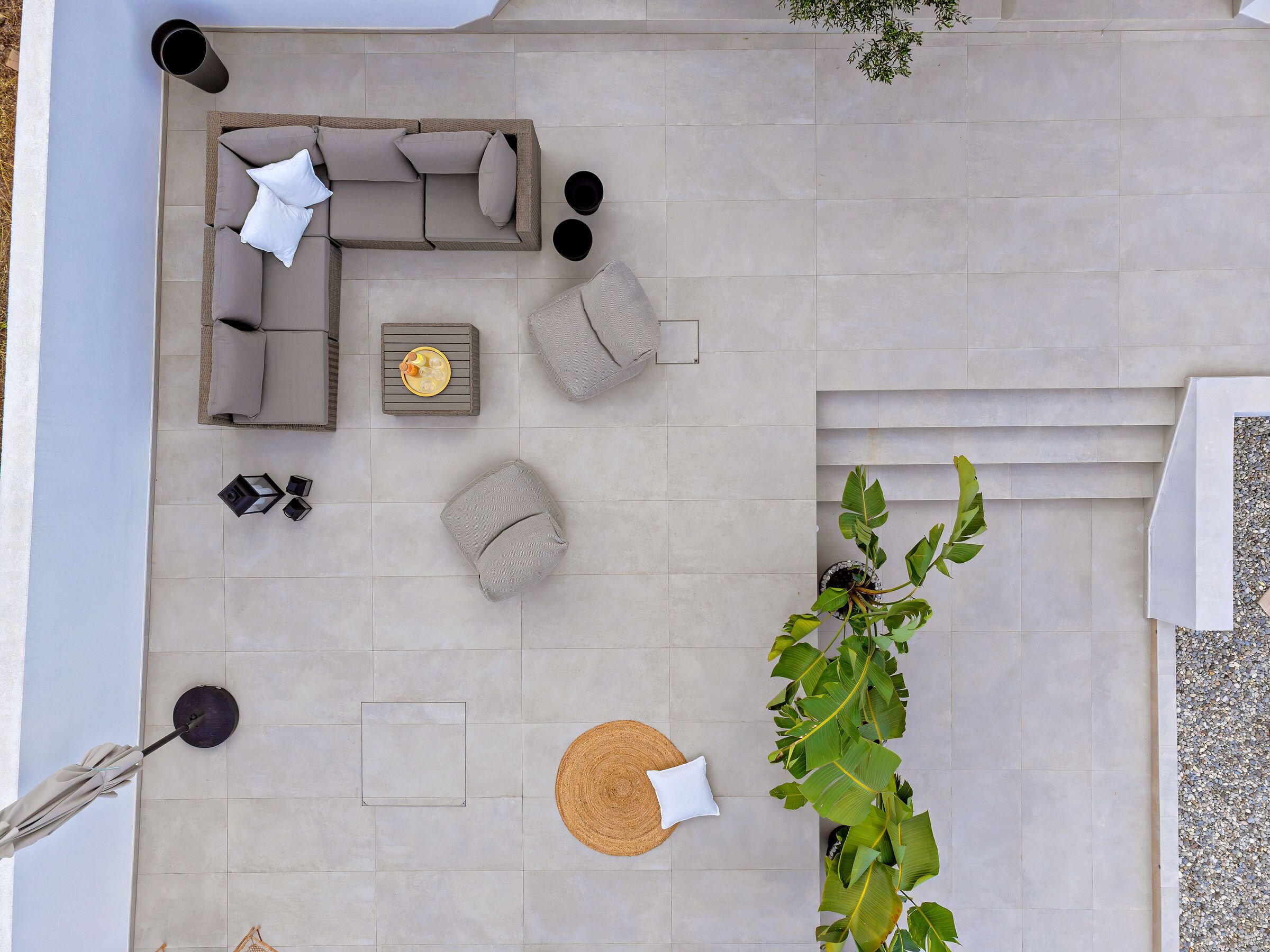 A top-down view of a modern outdoor seating area with a sofa, cushions, a small table with a fruit bowl, and a large plant.