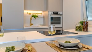 Een moderne keuken met een wit aanrecht, een glazen wijnglas, een schaal met eten en potten met kruiden.