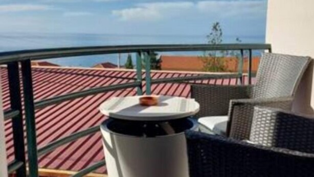 Un balcon avec une table et des chaises, une vue sur les immeubles et un ciel dégagé.