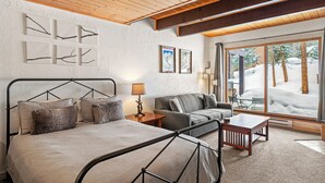 A cozy room with a bed, a sofa, a table, and a large window with a snowy view.