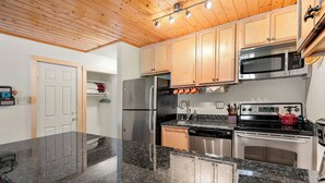 A modern kitchen with granite countertops, stainless steel appliances, wooden cabinets, and a wooden ceiling.