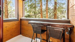 A wooden cabin with a built-in bench and two wicker chairs, a large window overlooking a forest. - Studio in Great Area, Easy Walk to Town & Peak 9 (Breckenridge)