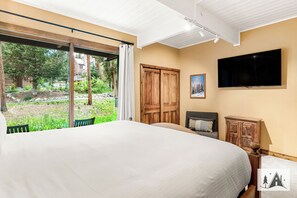 Ein Schlafzimmer mit einem großen Bett, einem an der Wand montierten Fernseher und einer Schiebetür zu einem Garten.