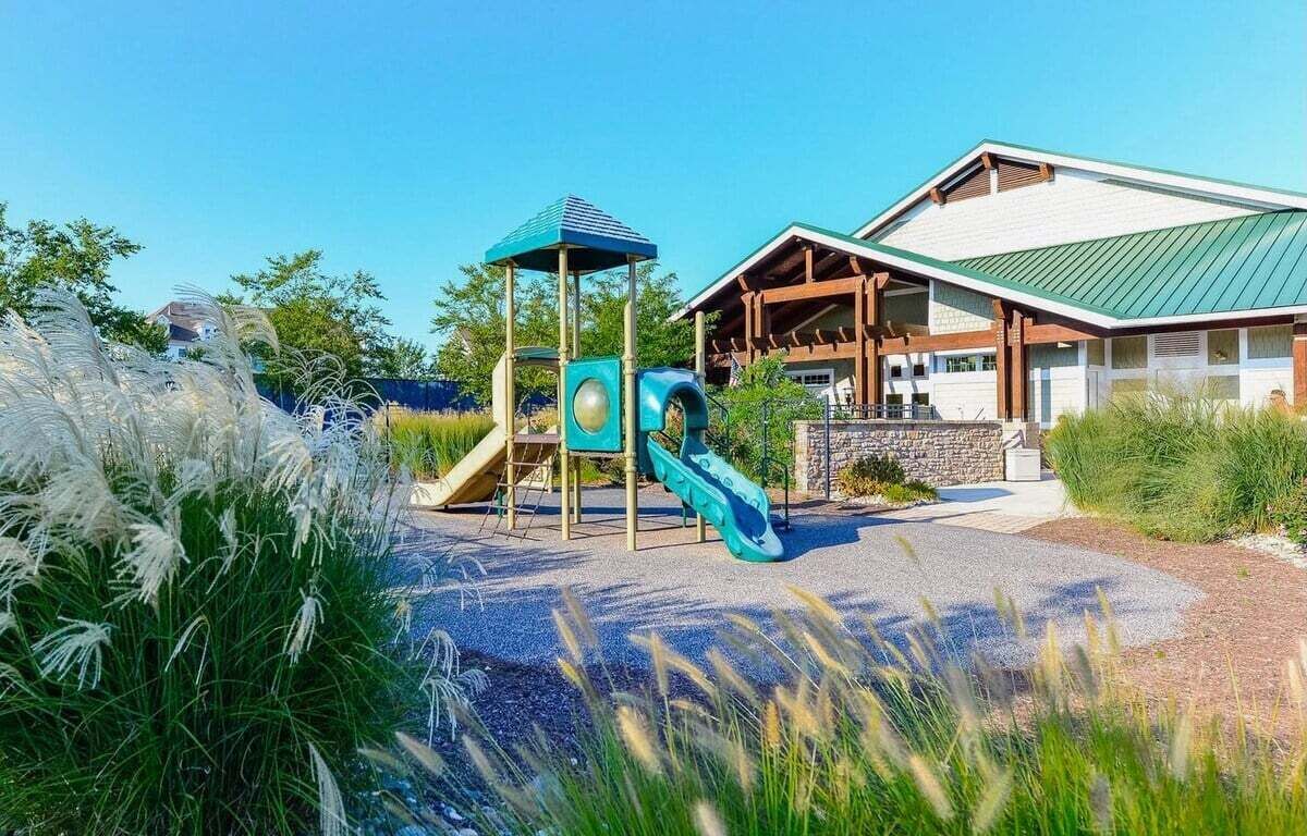Ein Spielplatz mit Rutsche und Klettergerüst, ein überdachter Spielbereich und ein Gebäude mit Gründach und Steinaußenwand.
