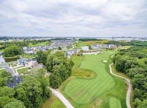 Un parcours de golf avec un obstacle d’eau, entouré de bâtiments résidentiels et d’une végétation luxuriante.