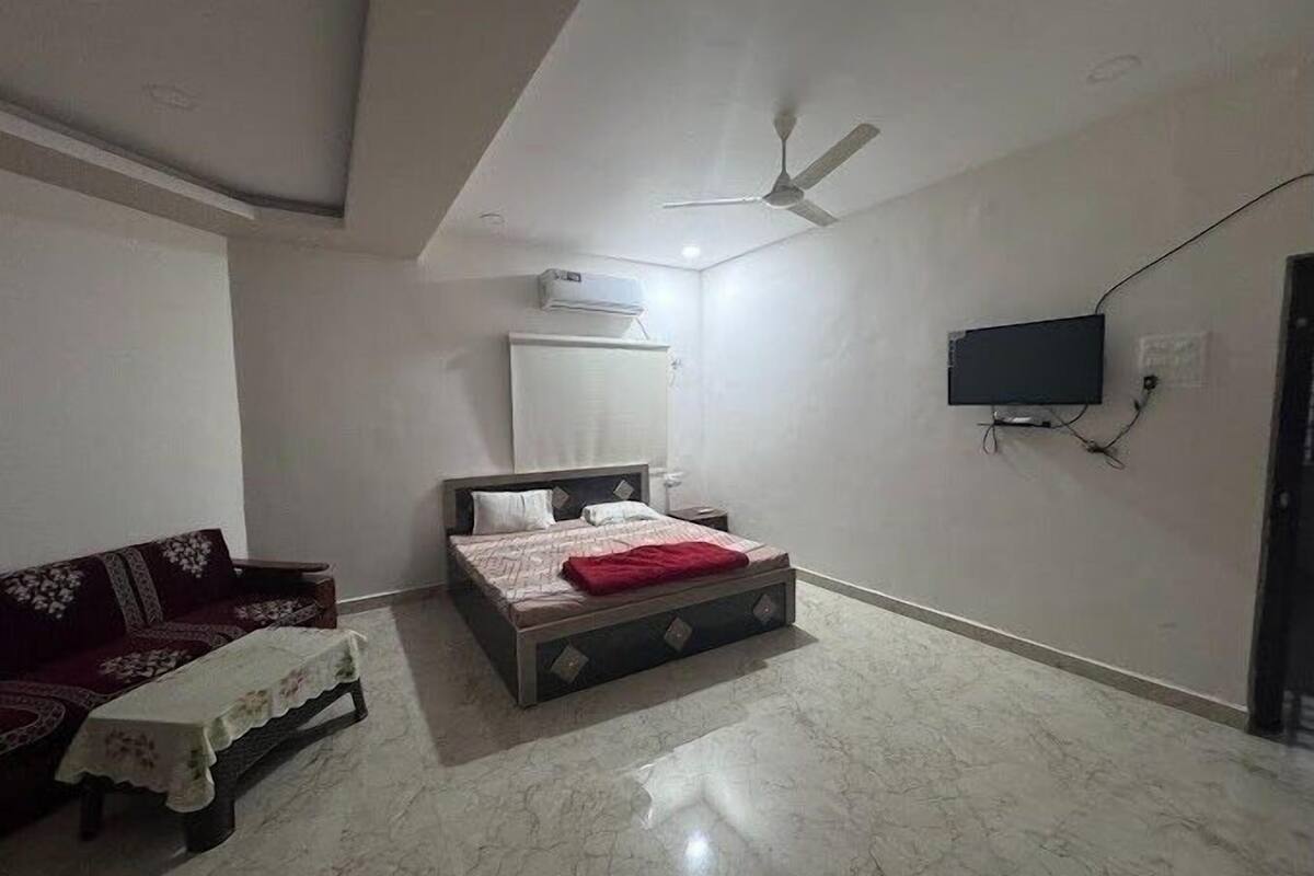 A bedroom with a bed, a ceiling fan, a TV mounted on the wall, and a sofa.