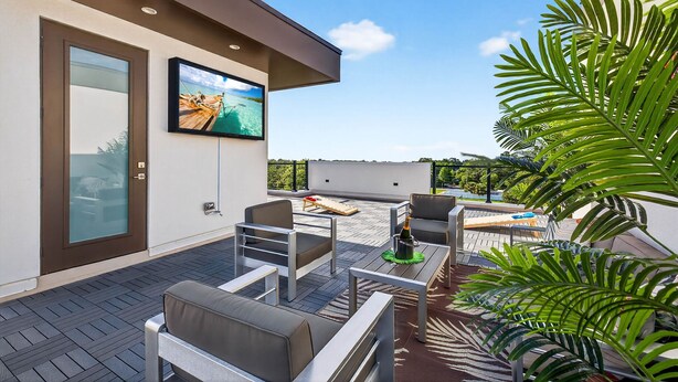 Um pátio externo moderno com televisão de tela plana, área de estar ao ar livre e vista para o céu e vegetação.