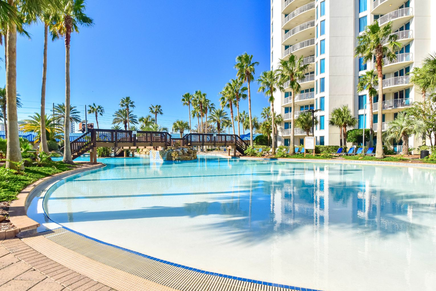 Ein großer Pool, umgeben von Palmen und einem mehrstöckigen Hotelgebäude.