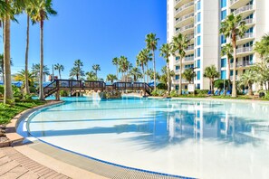 Une grande piscine entourée de palmiers et un immeuble d’hôtel à plusieurs étages.