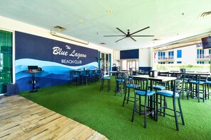 A beach-themed lounge area with a mural, multiple tables and chairs, and a ceiling fan. - 12th Floor Condo w/ Family Friendly Amenities at The Palms of Destin! 🌴🌊 (Destin)