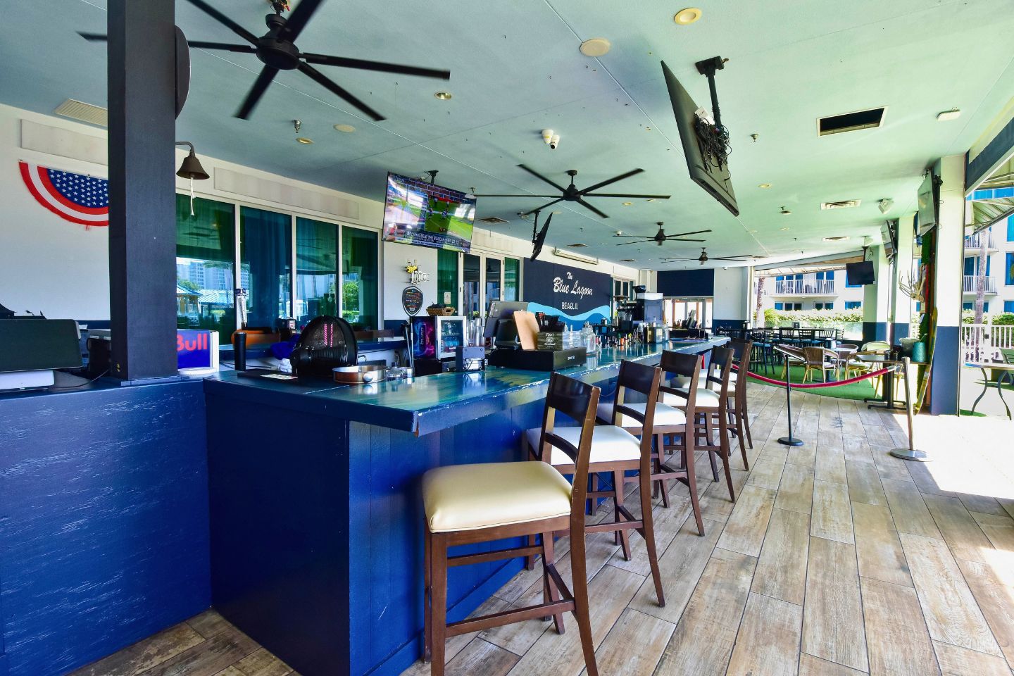 A bar area with a counter, multiple ceiling fans, and bar stools.