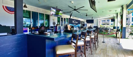 A bar area with a counter, multiple ceiling fans, and bar stools.