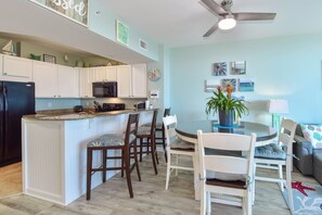 A modern kitchen with white cabinets, a black refrigerator, and a microwave. There is a dining area with a round table and chairs, and a ceiling fan above. - 12th Floor Condo w/ Family Friendly Amenities at The Palms of Destin! 🌴🌊 (Destin)