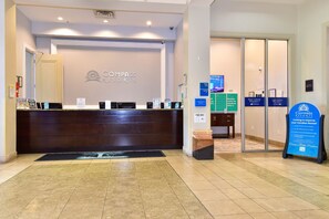 Un espace d’accueil comprenant un comptoir de réception, un panneau d’affichage et des panneaux de signalisation indiquant l’emplacement des différentes tours du bâtiment.