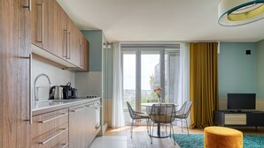 Eine moderne Küche mit Holzschränken, ein Essbereich mit rundem Tisch und Stühlen, ein Fernseher und ein Balkon mit Aussicht.
