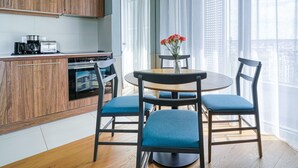 Une cuisine moderne avec des meubles en bois, un coin repas avec une table ronde et des chaises bleues, et une grande fenêtre ornée de rideaux légers.