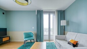 Un salon avec un canapé turquoise, un fauteuil turquoise, une table basse en bois, un téléviseur posé sur un meuble et une lampe sur pied.