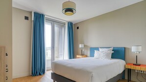 Une chambre d’hôtel avec un lit, deux tables de chevet, une fenêtre avec des rideaux, un luminaire au plafond et une vue sur l’extérieur.