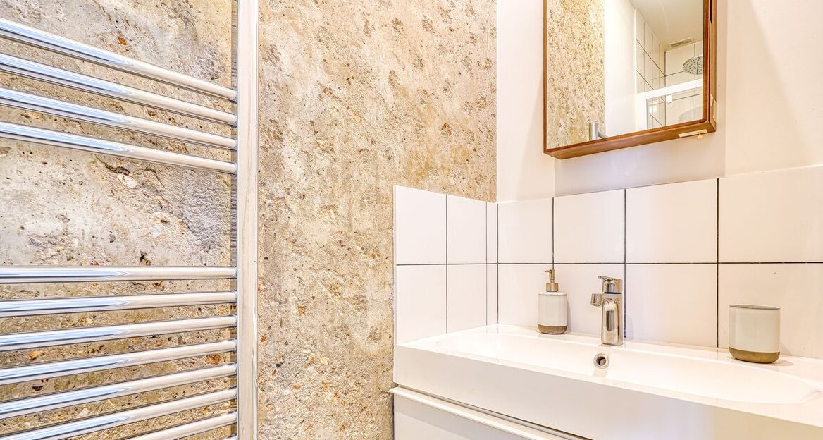 Un baño con pared de mármol, lavamanos blanco, espejo y toallero.