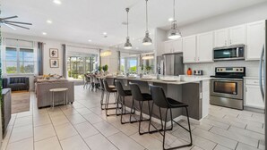A modern kitchen with white cabinets, stainless steel appliances, and a central island with bar stools. - 12BR, BBQ Oasis, Game Room & Home Theater! (Davenport)