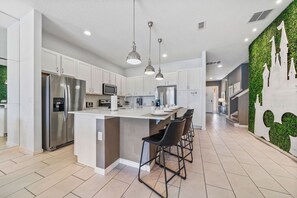 A modern kitchen with stainless steel appliances, a central island with bar stools, and a green wall feature. - 12BR, BBQ Oasis, Game Room & Home Theater! (Davenport)