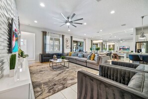 A modern living room with a sofa, coffee table, and a ceiling fan. - 12BR, BBQ Oasis, Game Room & Home Theater! (Davenport)