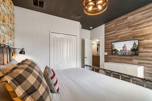 A bedroom with a large bed, a television mounted on the wall, and a wooden accent wall.