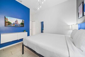 Ein Schlafzimmer mit einem großen Bett, einem weißen Kopfteil, einer blauen Akzentwand, einem Wand-Fernseher und einer weißen Tür.