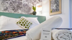 Una cama bien hecha con una toalla doblada, un cartel de bienvenida y una manta decorativa.