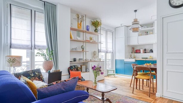 Una sala de estar moderna con un sofá azul, una mesa de centro y una estantería llena de objetos decorativos.