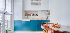 A modern kitchen with blue cabinets, a wooden dining table, and a fruit bowl.