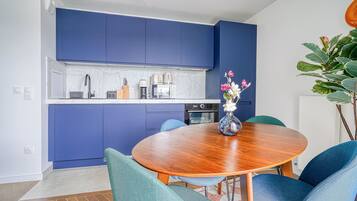 A modern kitchen with blue cabinets, a round wooden dining table, and teal chairs.