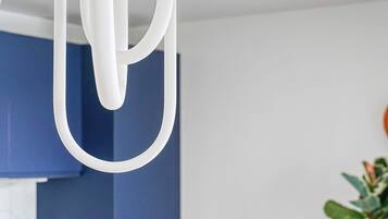 Une cuisine moderne avec des meubles bleus, un luminaire suspendu blanc et un coin repas comprenant une table en bois et des chaises vertes.