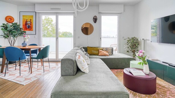 Una sala de estar moderna con un sofá gris, una mesa de centro redonda y un comedor con sillas azules.