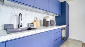 Una cocina moderna con armarios azules, encimera de mármol, un lavabo, cafetera y tostadora.