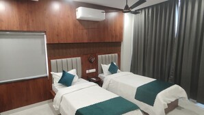 A hotel room with two beds, a large mirror, an air conditioning unit, a ceiling fan, and a view of the outside through a window with curtains. - Vaishnavi Inn (Rajahmundry)