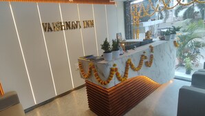 A reception desk with a marble top, a sign above it, and a view of the outside through a glass window. - Vaishnavi Inn (Rajahmundry)