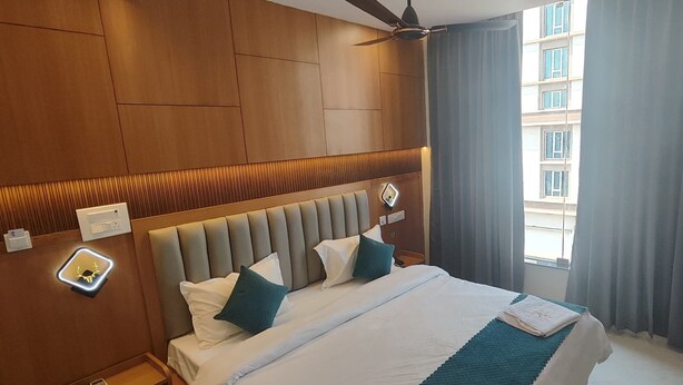 A hotel room with a large bed, wooden paneling on the walls, a ceiling fan, and a view of a building through the window. - Vaishnavi Inn (Rajahmundry)